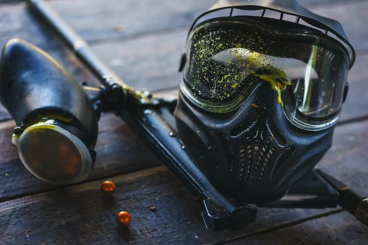 Paint-splattered mask and marker with two paintballs on a table
