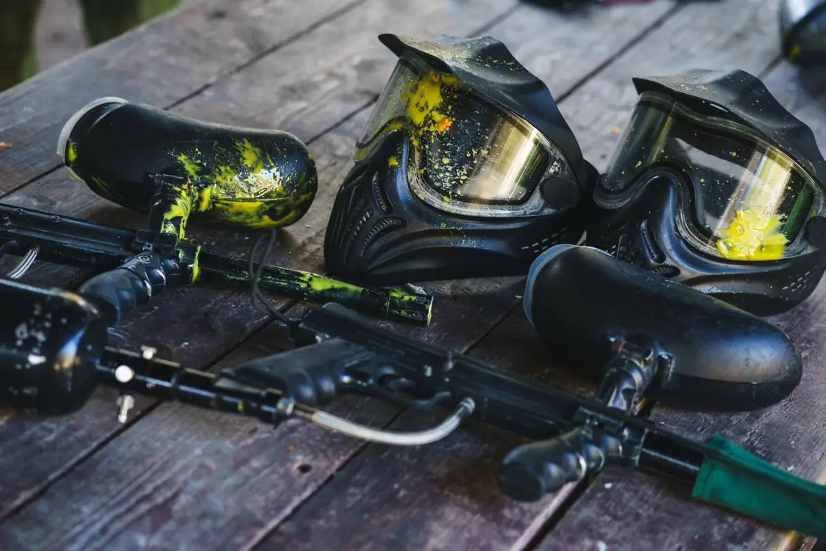 Rental paintball markers and masks splattered with yellow paint on a wooden table