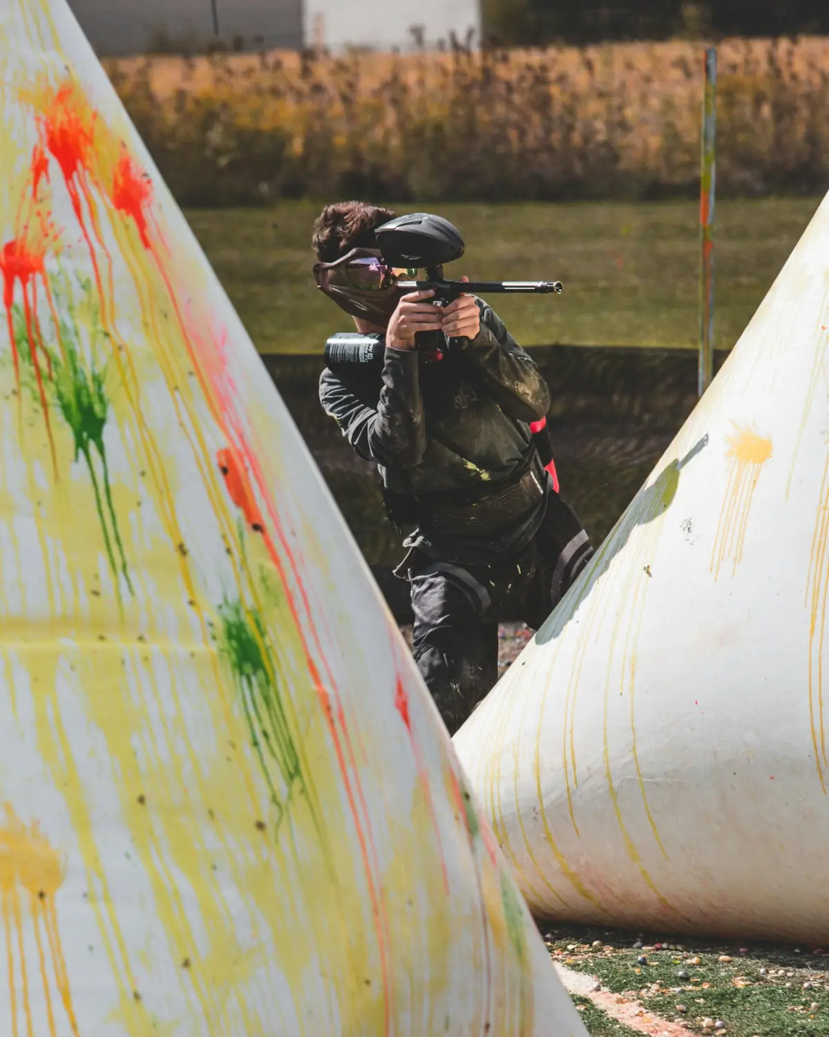 Player aiming between paint-splattered inflatable bunkers on the turf speedball field