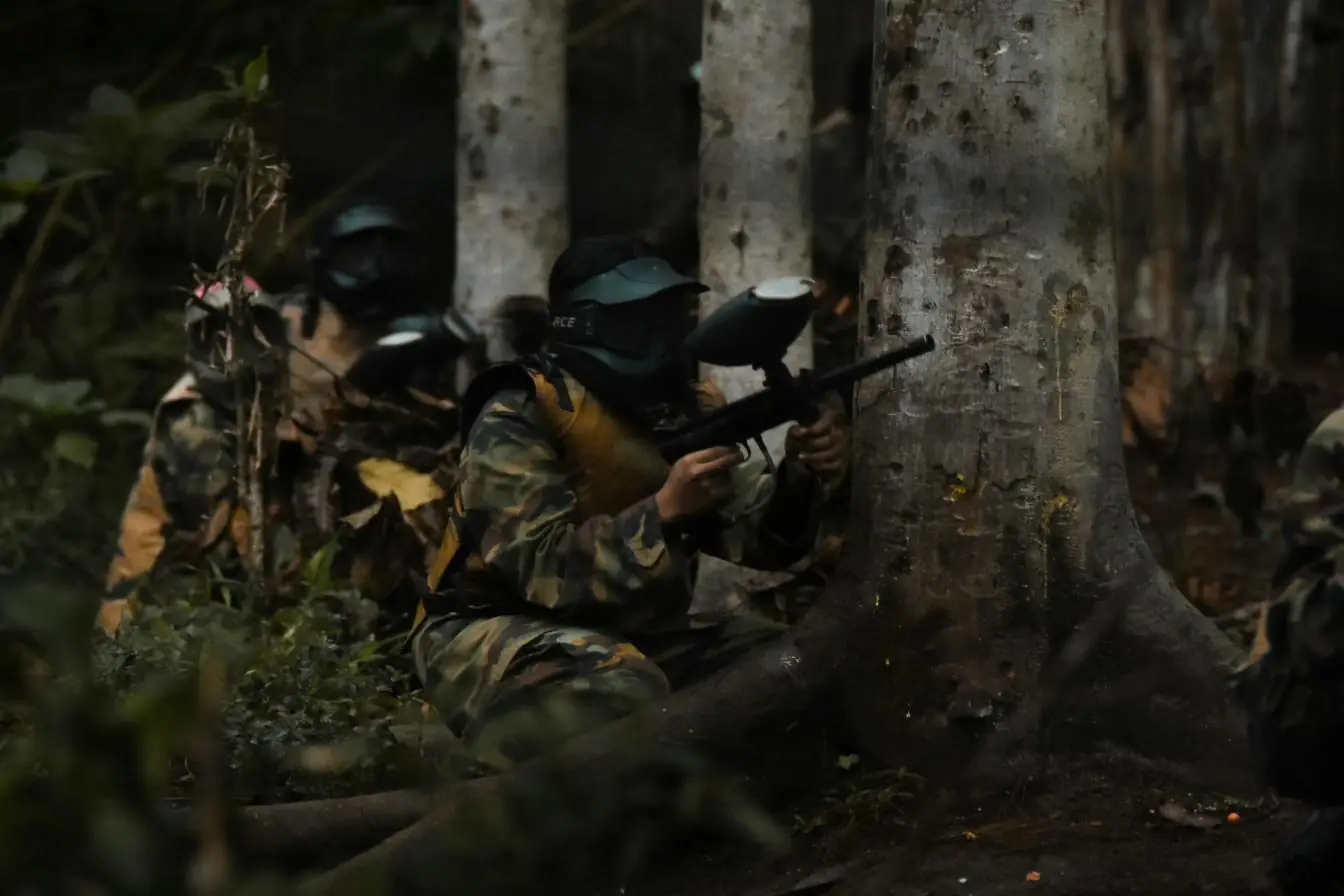 Woodsball players in camouflage advancing between trees